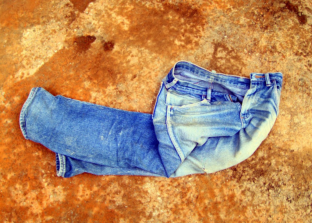 A pair of faded jeans is shown laying on a carpeted floor. 